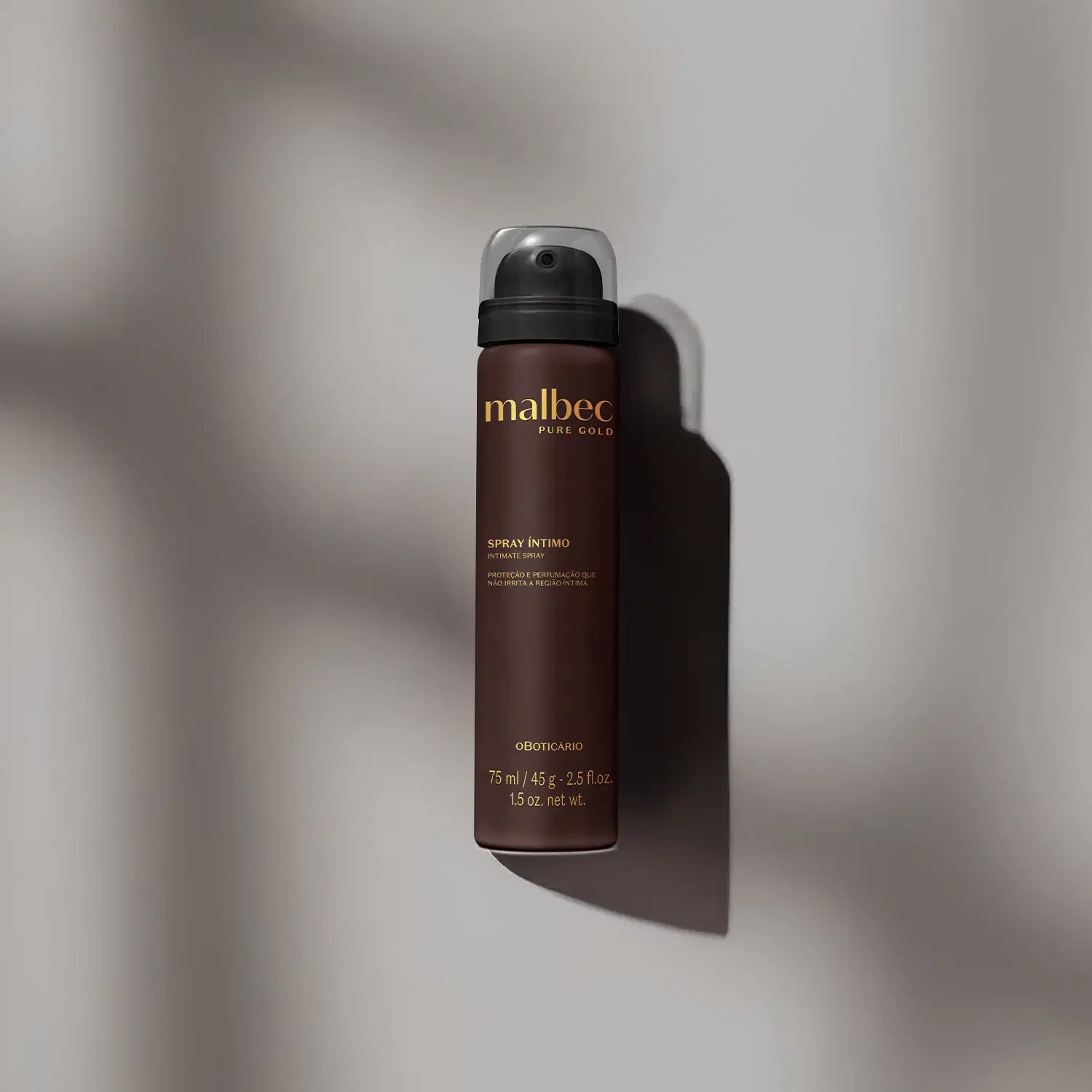 Imagem de um frasco de spray íntimo da marca Malbec Pure Gold em fundo cinza, com sombras projetadas, em ambiente minimalista e monocromático.