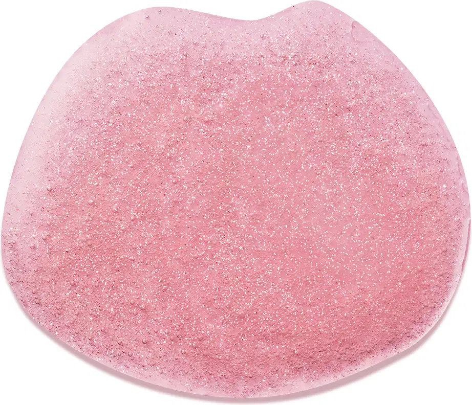 Objeto de perfumaria com textura granulada e brilhante em tom de rosa. Superfície irregular e aspecto cristalino, sugerindo uma composição sólida e possivelmente relacionada a produtos de beleza.