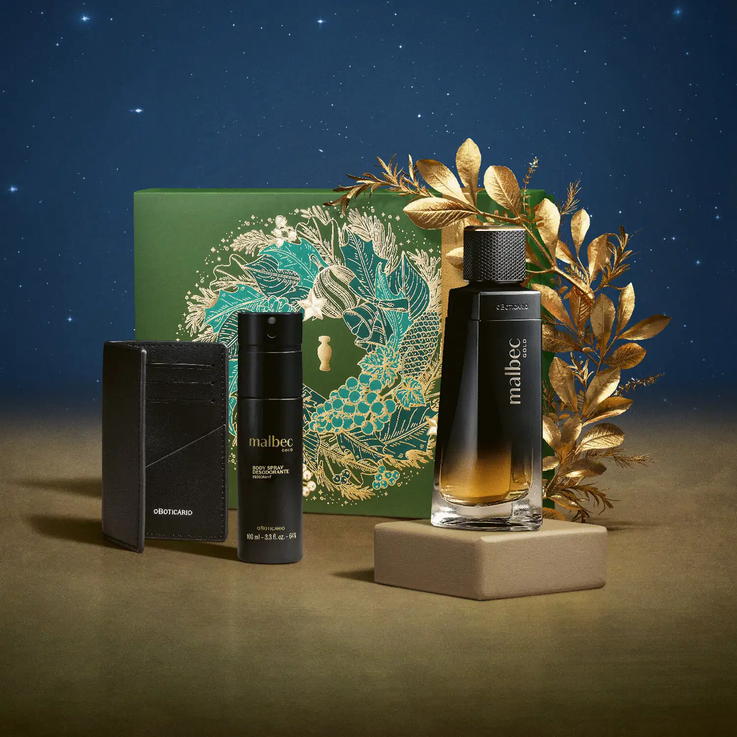 Imagem do Kit Presente Natal Malbec Gold mostra o frasco preto fosco de desodorante colônia em um pedestal bege e os demais itens do kit em uma sobre superfície marrom e fundo azul , com um cipestre dourado adornando a caixa.