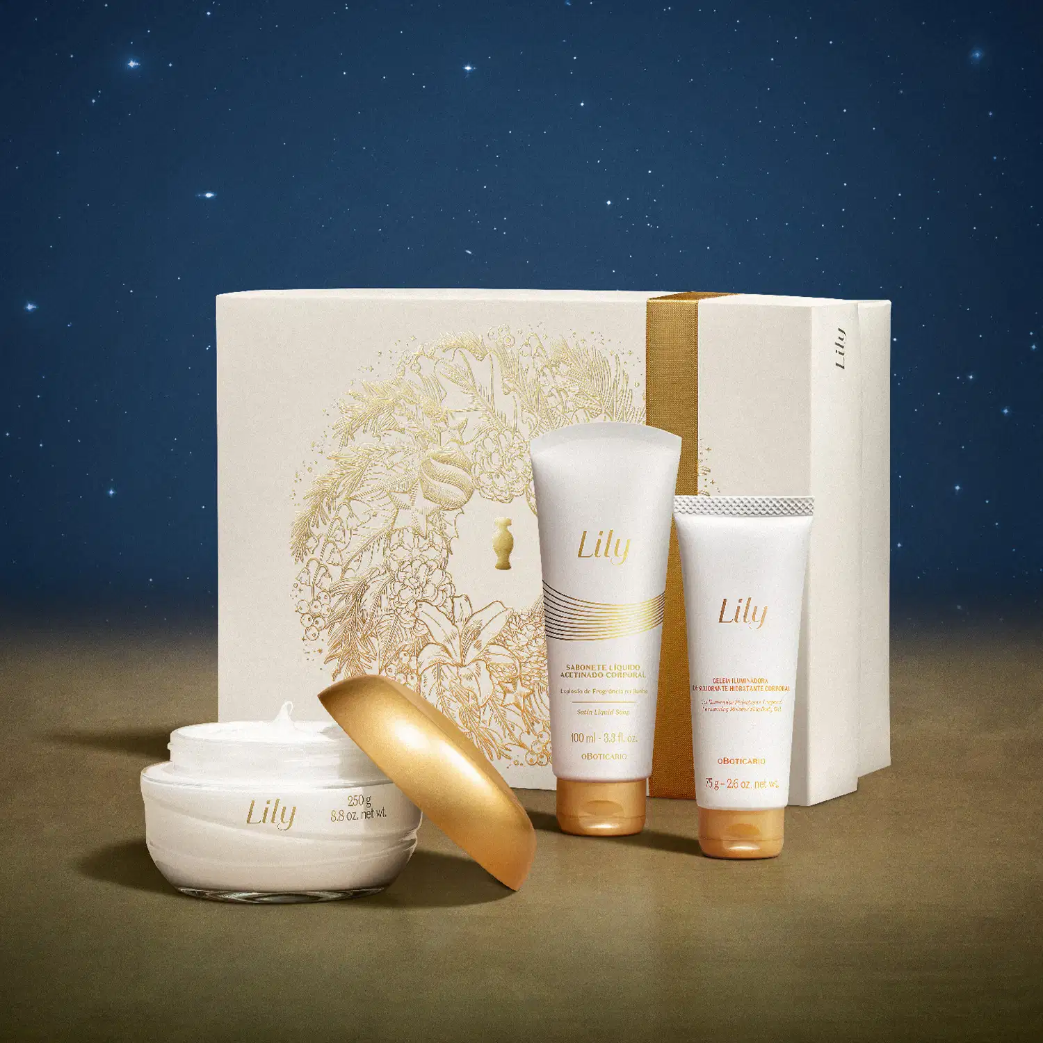 Imagem do Kit Presente Natal Lily com pote de creme hidratante corporal, duas bisnagas, sendo uma de sabonete líquido e outra de geleia corporal e uma caixa presenteável rosa-claro com ilustração floral em cenário com superfície marrom e fundo azul.