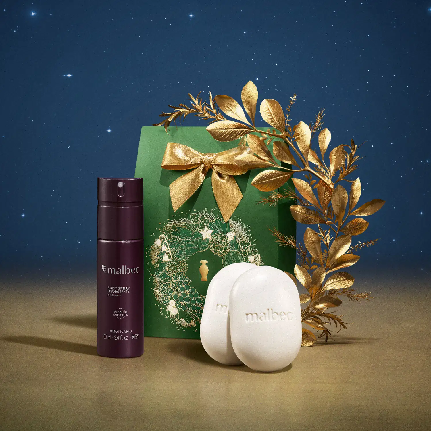 Imagem do Kit Presente Natal Malbec Cuidados com frasco vinho e cinza de body spray, dois sabonetes em barra brancos e uma sacola presenteável verde com estampa natalina em cenário com superfície marrom e fundo azul-escuro, simulando um céu estrelado.