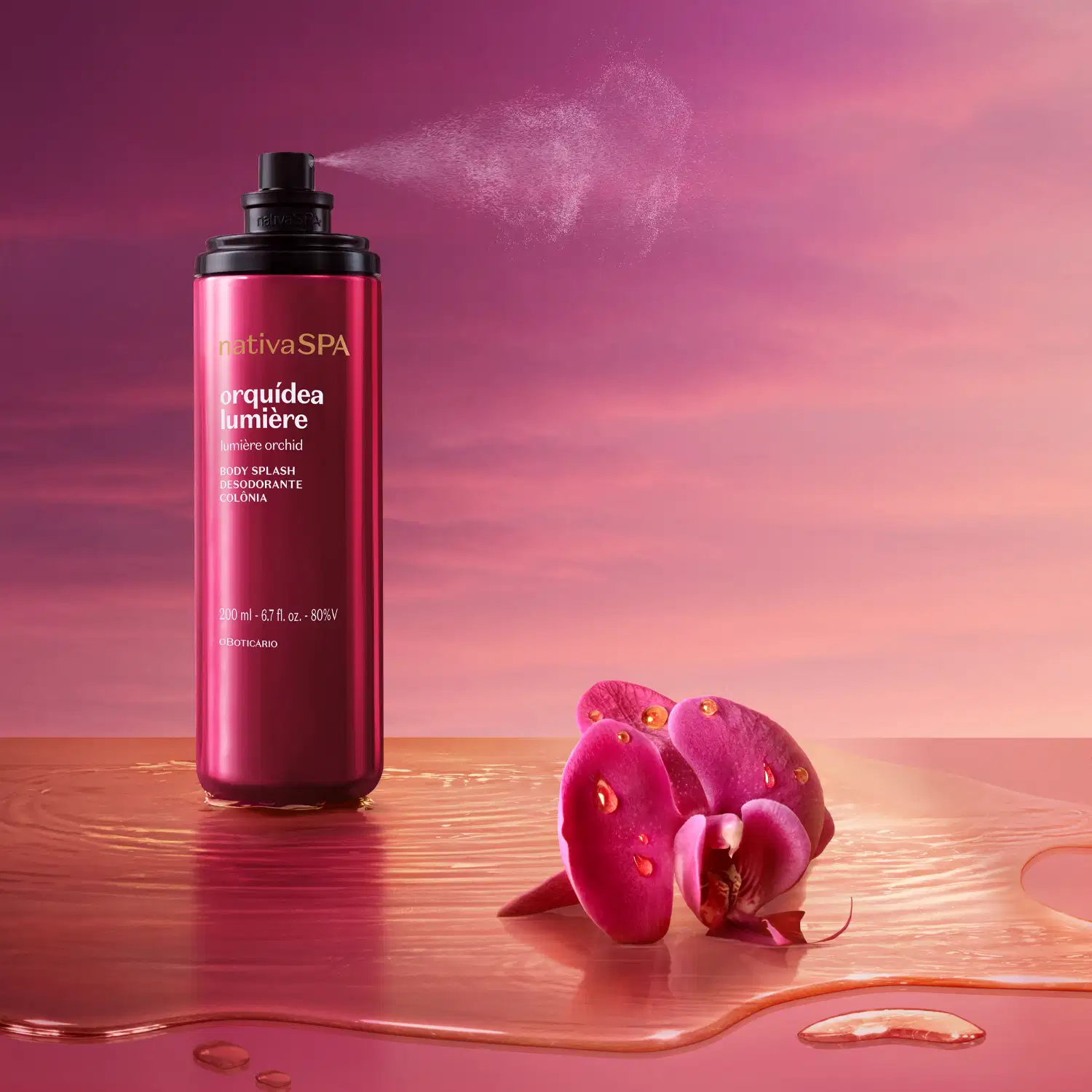 Frasco de item de perfumaria da marca Nativa SPA Orquídea Lumiere aberto e da válvula spray vemos sair uma bruma do produto. O frasco na cor rosa está sobre superfície rosa molhada e ao lado, uma orquídea rosa contra um céu rosa e laranja.