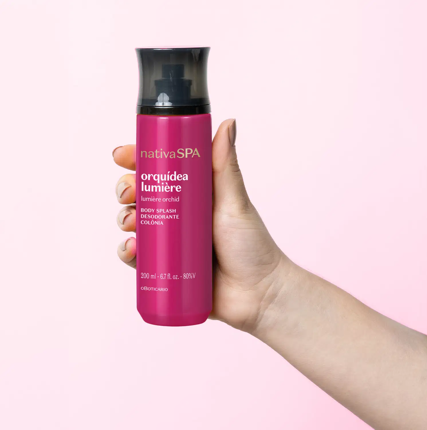 Frasco cilíndrico de item de perfumaria da marca Nativa SPA Orquídea Lumière, na cor rosa vibrante, sendo segurado por uma mão feminina contra um fundo rosa claro.