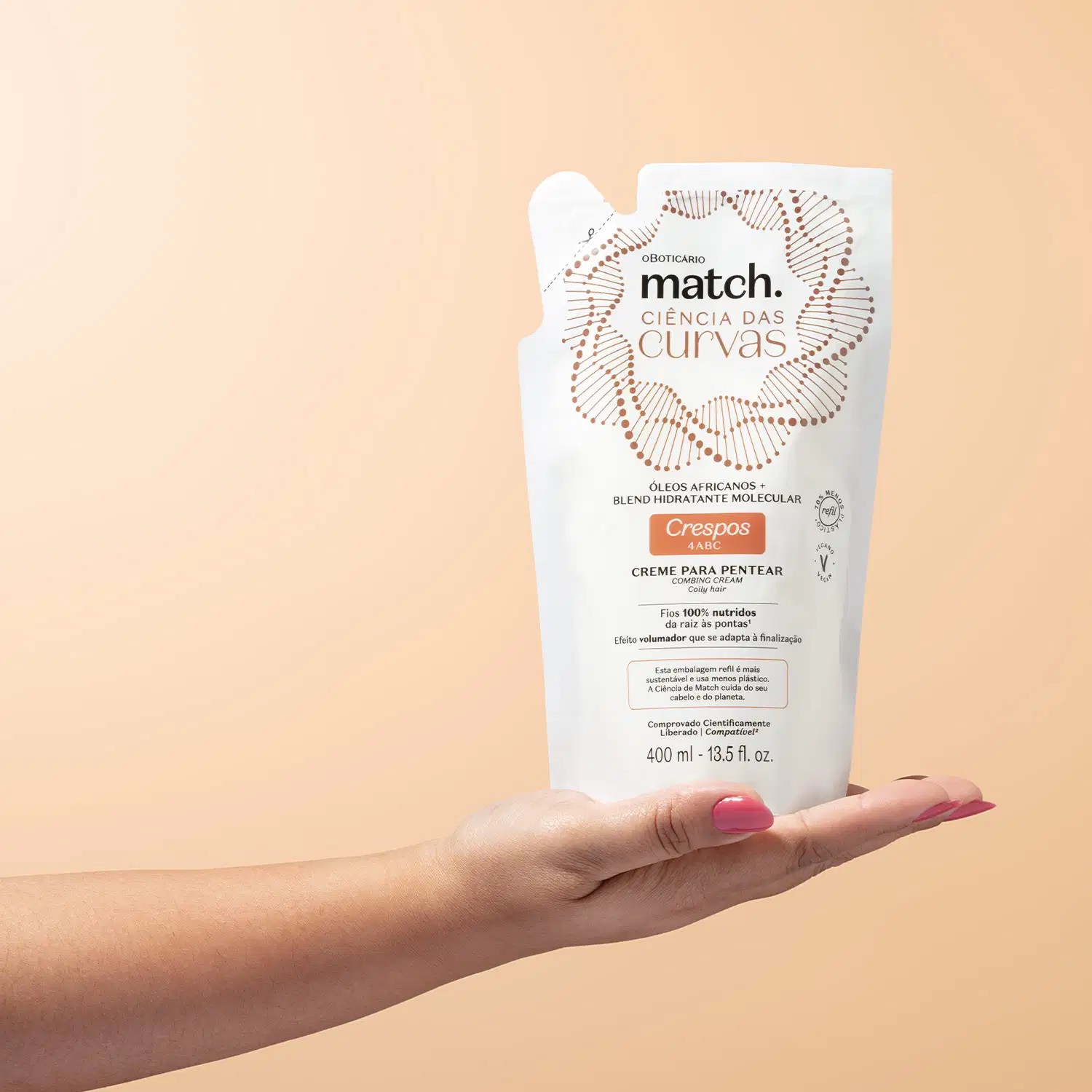 Imagem de uma mão segurando uma embalagem refil branca de creme para pentear da marca Match, com design de círculos e linhas em marrom, informando "Ciência das Curvas" e "Crespos 4ABC" no rótulo. O fundo é rosa bem claro.