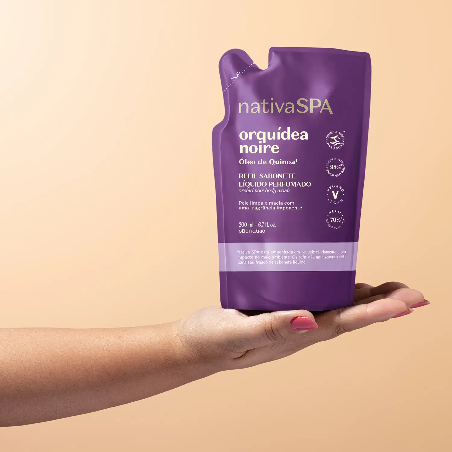 Imagem de uma mão segurando um refil de sabonete líquido Nativa SPA Orquídea Noire em sachê roxo com letras douradas e brancas em fundo bege.