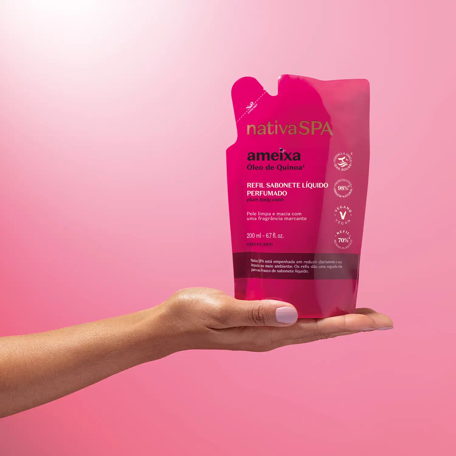 Imagem de uma mão segurando um refil de sabonete líquido perfumado da marca Nativa SPA Ameixa em sachê na cor rosa vibrante e letras pretas e brancas, em fundo rosa.
