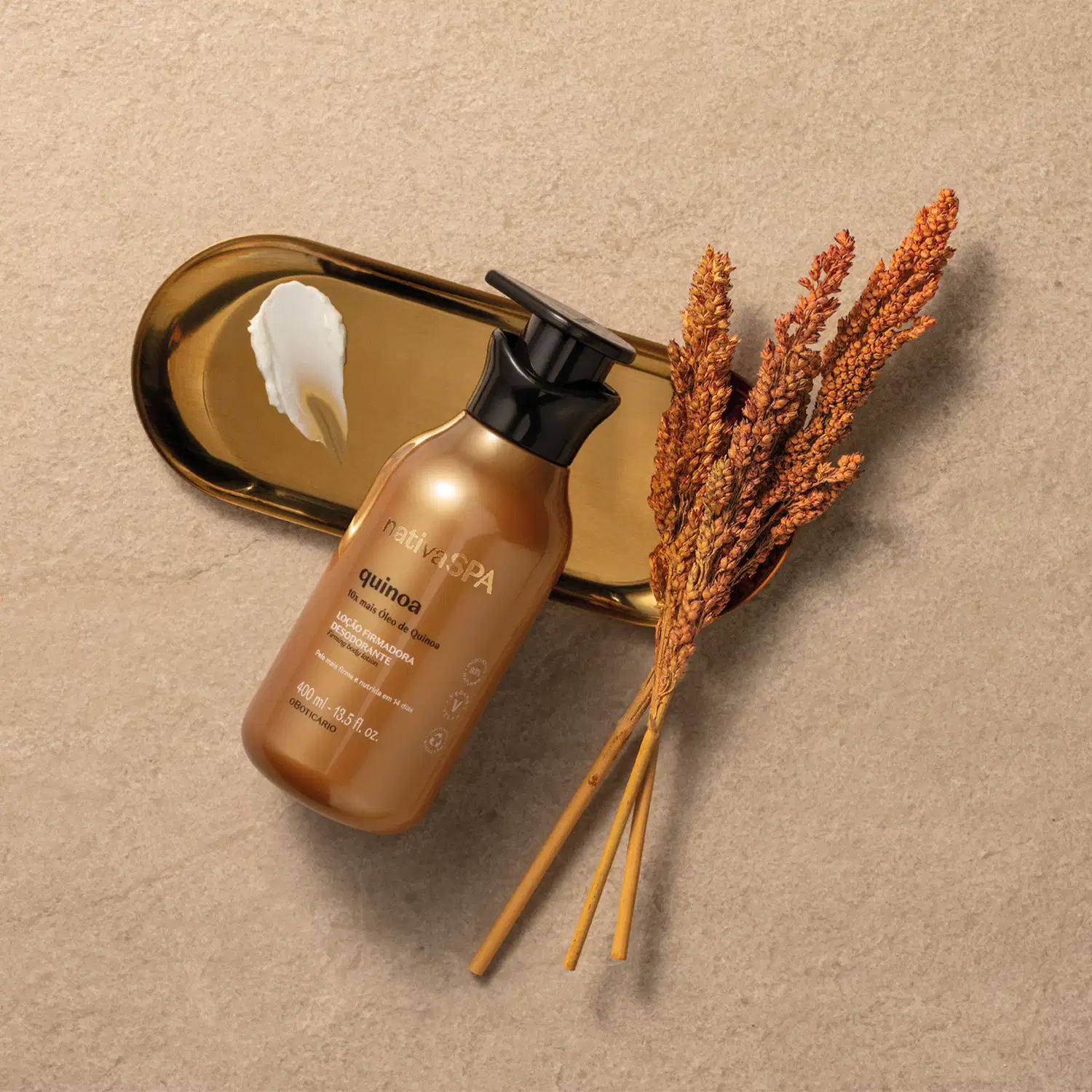 Imagem de um frasco de loção firmadora corporal da marca Nativa SPA Quinoa apoiado sobre superfície bege com espelho dourado, ao lado de hastes de trigo.