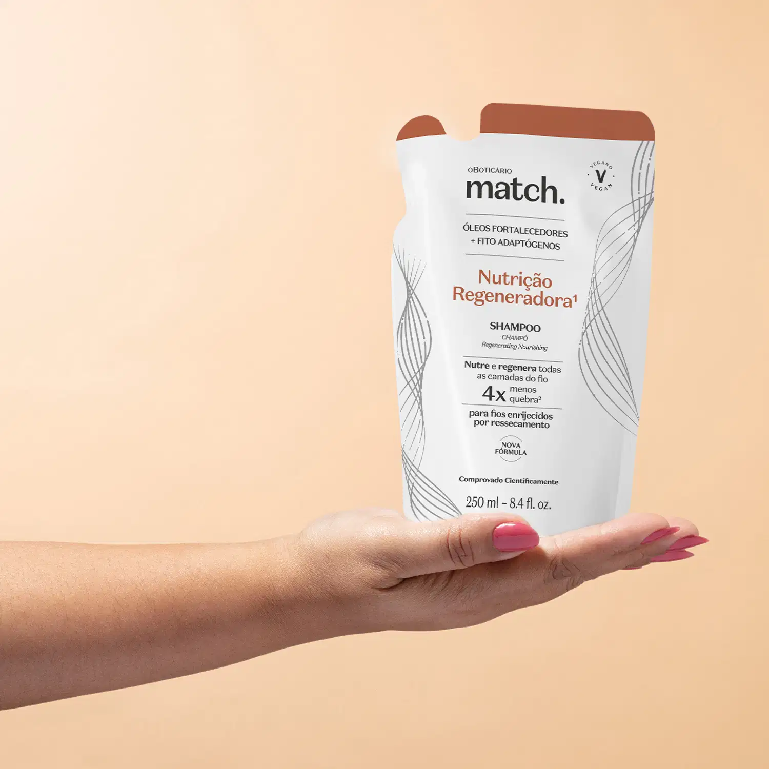 Imagem de uma mão feminina segurando um refil em forma de sachê na cor branca com detalhes laranja e letras pretas contendo shampoo da marca Match. Nutrição Regeneradora. O fundo da imagem é rosa.