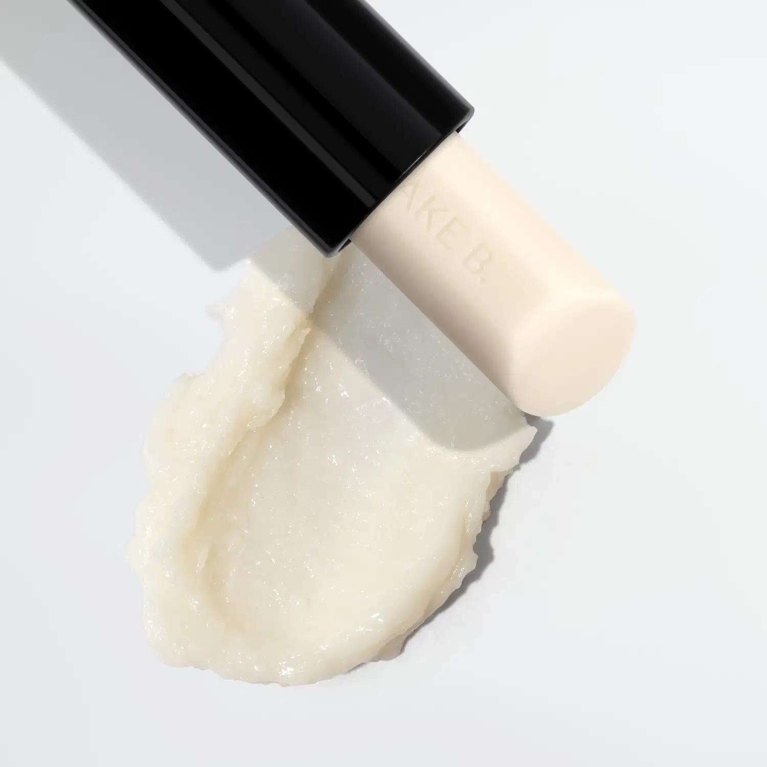Frasco preto de Balm Labial Noturno Make B. Lip Chronology Night Peeling., contendo produto de textura cremosa e brilhante em tom bege claro.