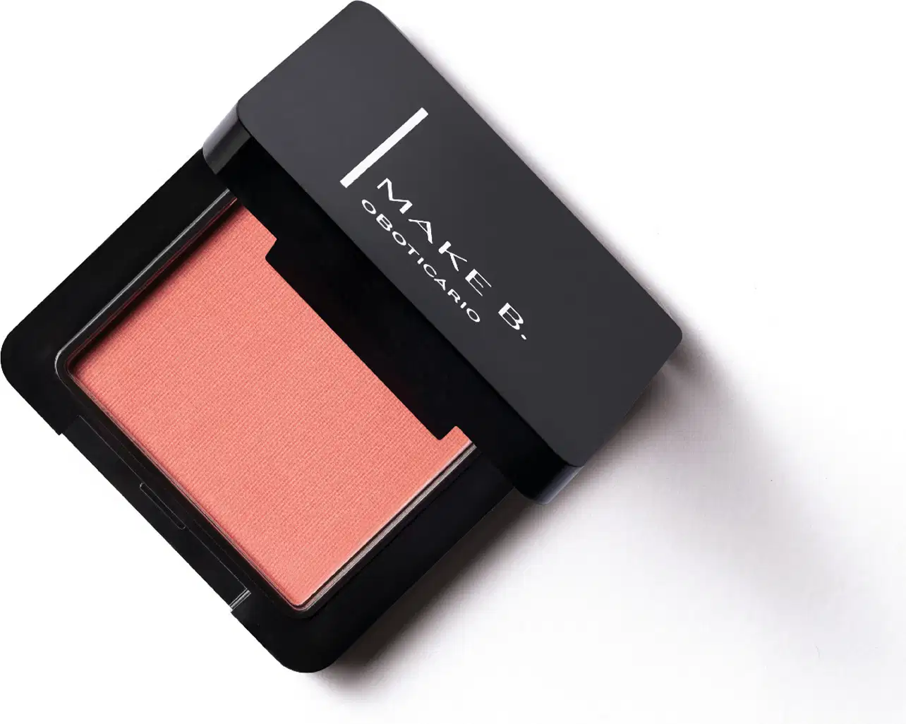 Embalagem preta de blush compacto da marca Make B. aberta, com formato quadrado, e dentro, vemos o produto de tonalidade coral vibrante.