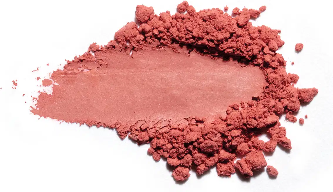 Textura de pó rosa-avermelhado com acabamento acetinado e superfície irregular, espalhada sobre fundo branco.