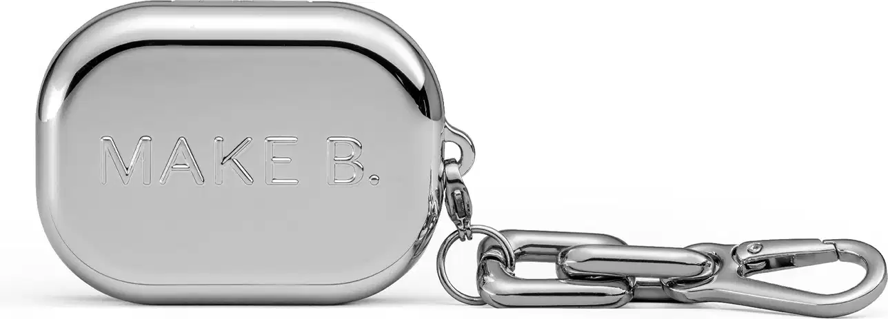 A imagem mostra a caixa do blush compacto em metal prateado com o texto "Make B." gravado, com um gancho de metal para pendurar. O possui uma aparência minimalista e elegante.