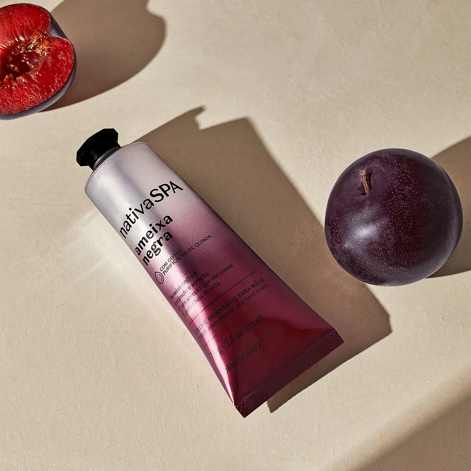 Tubo de creme hidratante para mãos da marca Nativa SPA da linha Ameixa Negra em tons degradê do roxo ao prata, com uma ameixa roxa inteira e outra cortada ao meio sobre superfície clara.