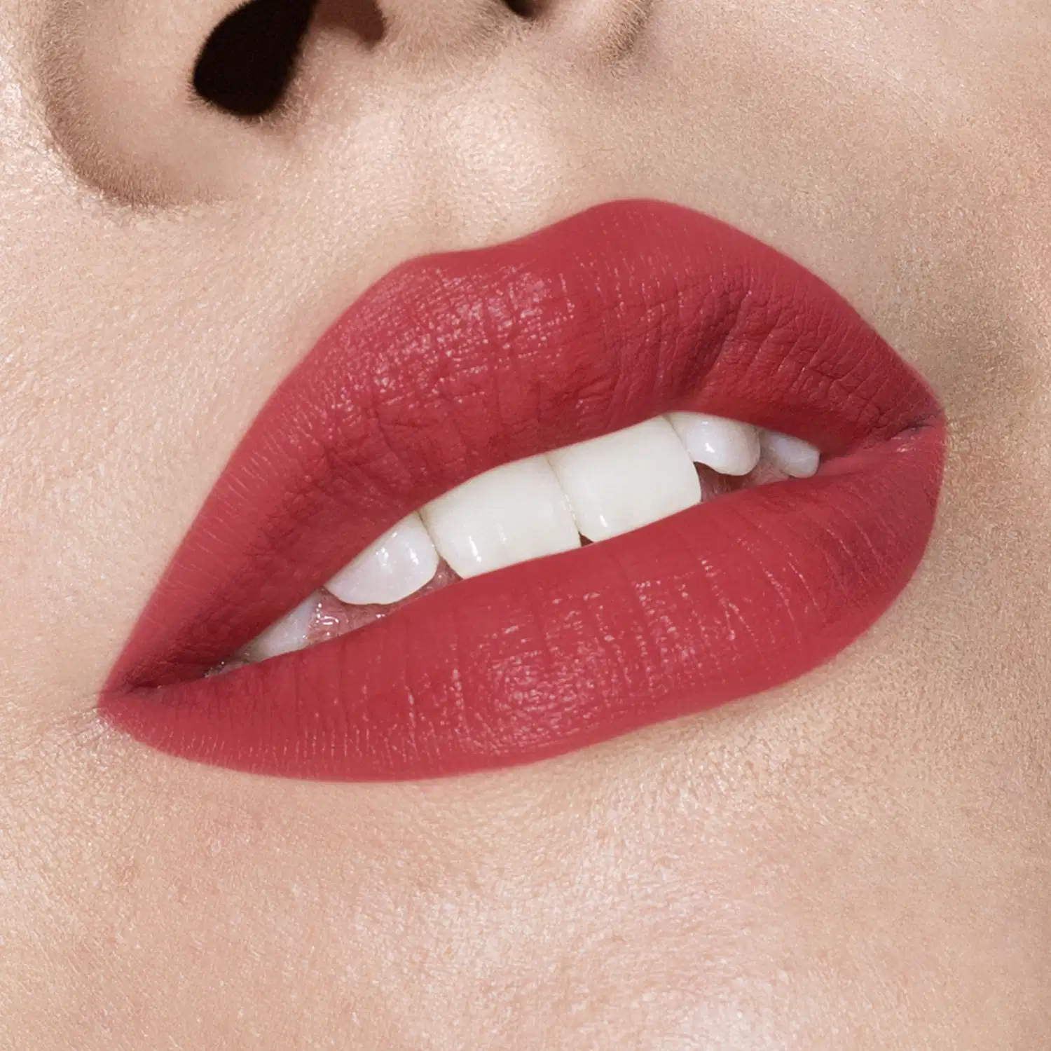 Imagem de lábios femininos em close-up com batom vermelho intenso. A boca tem um leve sorriso e está entreaberta, mostrando parcialmente os dentes brancos.