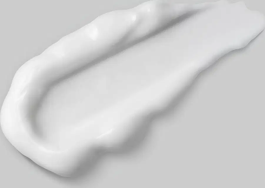 Imagem de um pouco de condicionador sobre superfície clara, lisa e uniforme, evidenciando a textura cremosa na cor branca do produto, que tem aparência suave e brilhante,