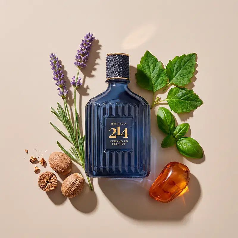Imagem de um ambiente elegante com elementos naturais, como folhas verdes, flores de lavanda e nozes, que complementam a embalagem da marca Botica 214, em tons azulados, sugerindo um contexto de fragrância inspirada na natureza.