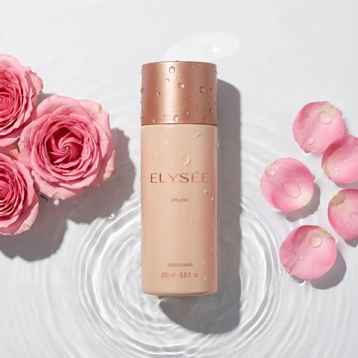 Frasco de item de perfumaria da marca Elysée sobre espelho d'água e com aspecto molhado. Ao redor 3 rosas e suas pétalas espalhadas sobre o espelho d'água, que forma círculos concêntricos denotando movimento.