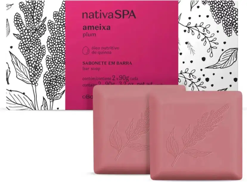 Imagem de uma caixa com faixa rosa e ilustrações em preto e branco de folhas e flores, contendo dois sabonetes em barra de cor rosa com formato quadrados. O produto é da marca Nativa SPA Ameixa Plum.