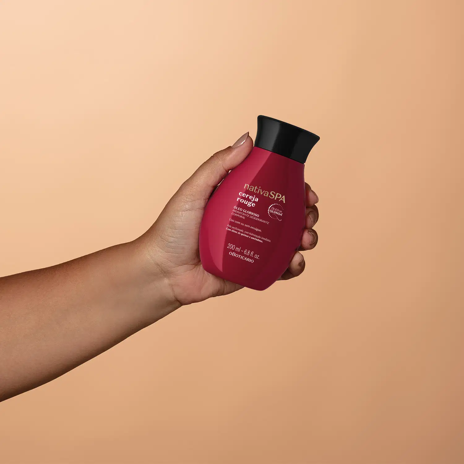 Imagem de um frasco de óleo glorioso corporal da marca Nativa SPA Cereja Rouge, em tom vermelho-escuro, sendo segurado por uma mão em fundo em tons de roxo.
