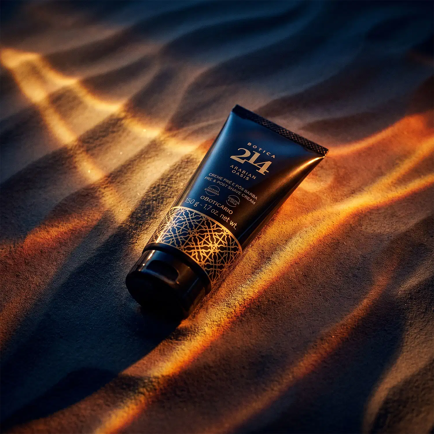 Tubo preto de item de cuidados com a pele pós-barba da linha Botica 214 Arabian Oasis em primeiro plano sobre uma superfície de areia ondulada, com fundo desfocado feixes de luzes douradas que criam um ambiente misterioso e dramático.