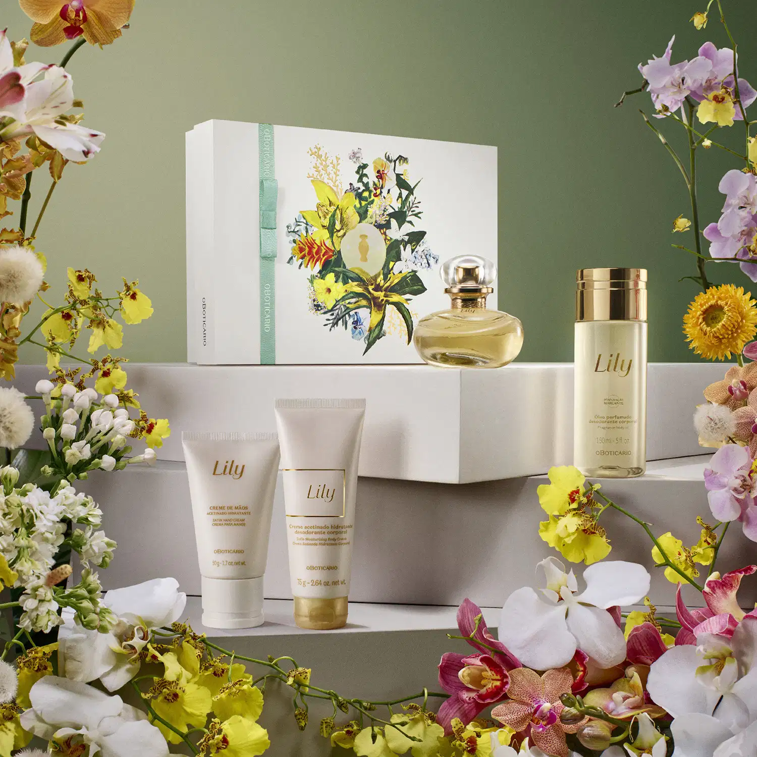 Imagem do kit Lily. sendo um creme para as mãos, uma loção corporal, um óleo corporal, eau de parfumuma caixa com ilustrações florais. O cenário conta com orquídeas amarelas e brancas e o kit está em cima de caixas brancas com fundo cinza.