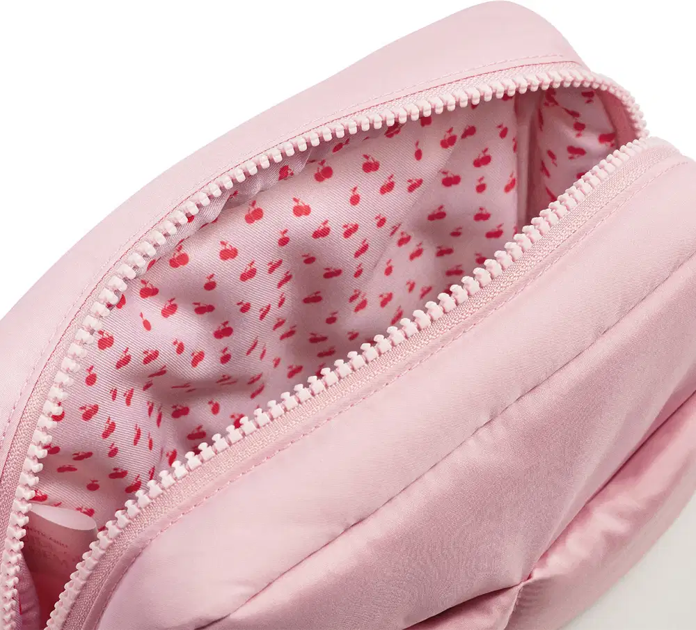 Imagem de nécessaire rosa com zíper, com estampa de cereja vermelha no interior. Sem rótulos ou marcas visíveis. Objeto compacto e portátil.