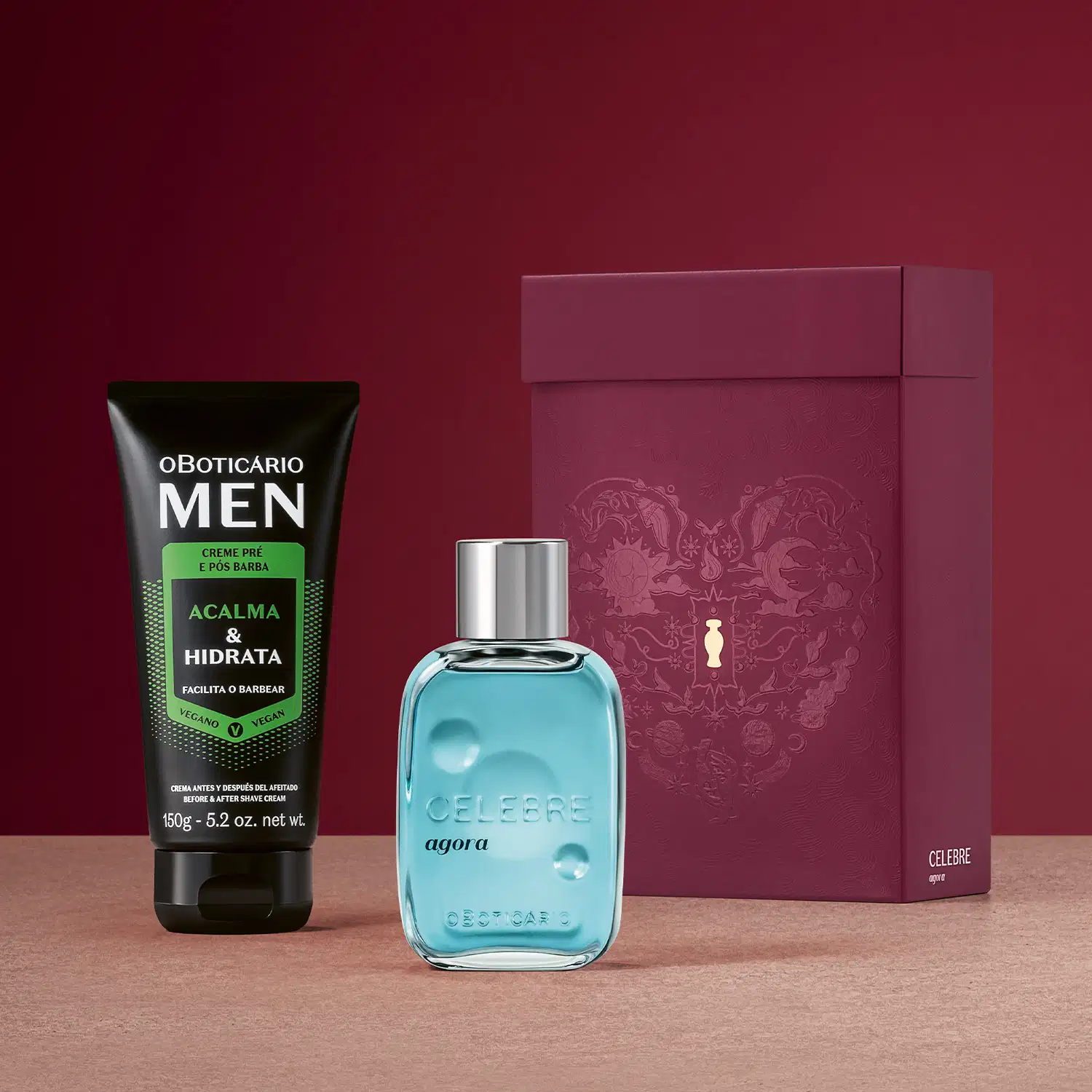 Caixa de presente de cor vinho com coração e ilustrações de temática celestial, item de perfumaria azul-turquesa com tampa prateada com a palavra CELEBRE em relevo no vidro, e uma bisnaga preta de creme da linha MEN sobre fundo bordô e superfície rosa.
