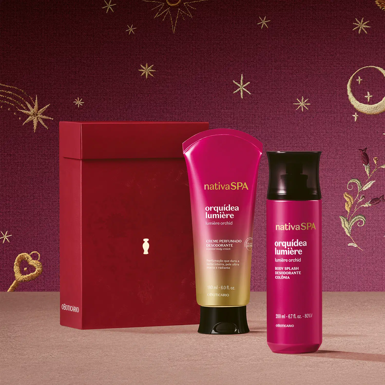Caixa de presente de cor vinho ao lado de uma bisnaga de creme corporal perfumado e body spray, ambos da marca Nativa SPA Orquídea Lumière na cor-de-rosa com tampa preta sobre superfície rosa claro e fundo rosa escuro com bordados celestiais dourados.