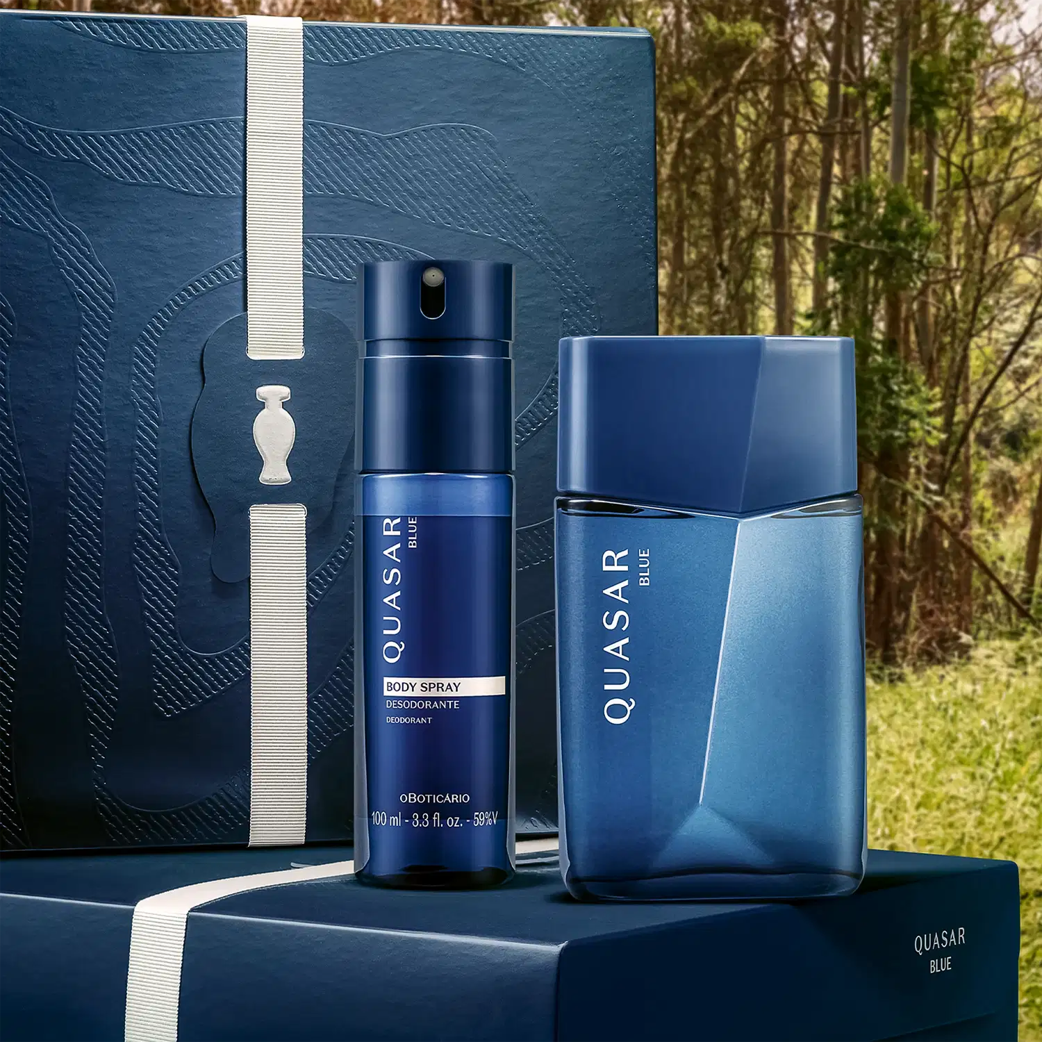 Conjunto de embalagens azuis de item de perfumaria da marca Quasar, incluindo frasco de desodorante spray e frasco de perfume, dispostos sobre superfície com fundo de floresta.