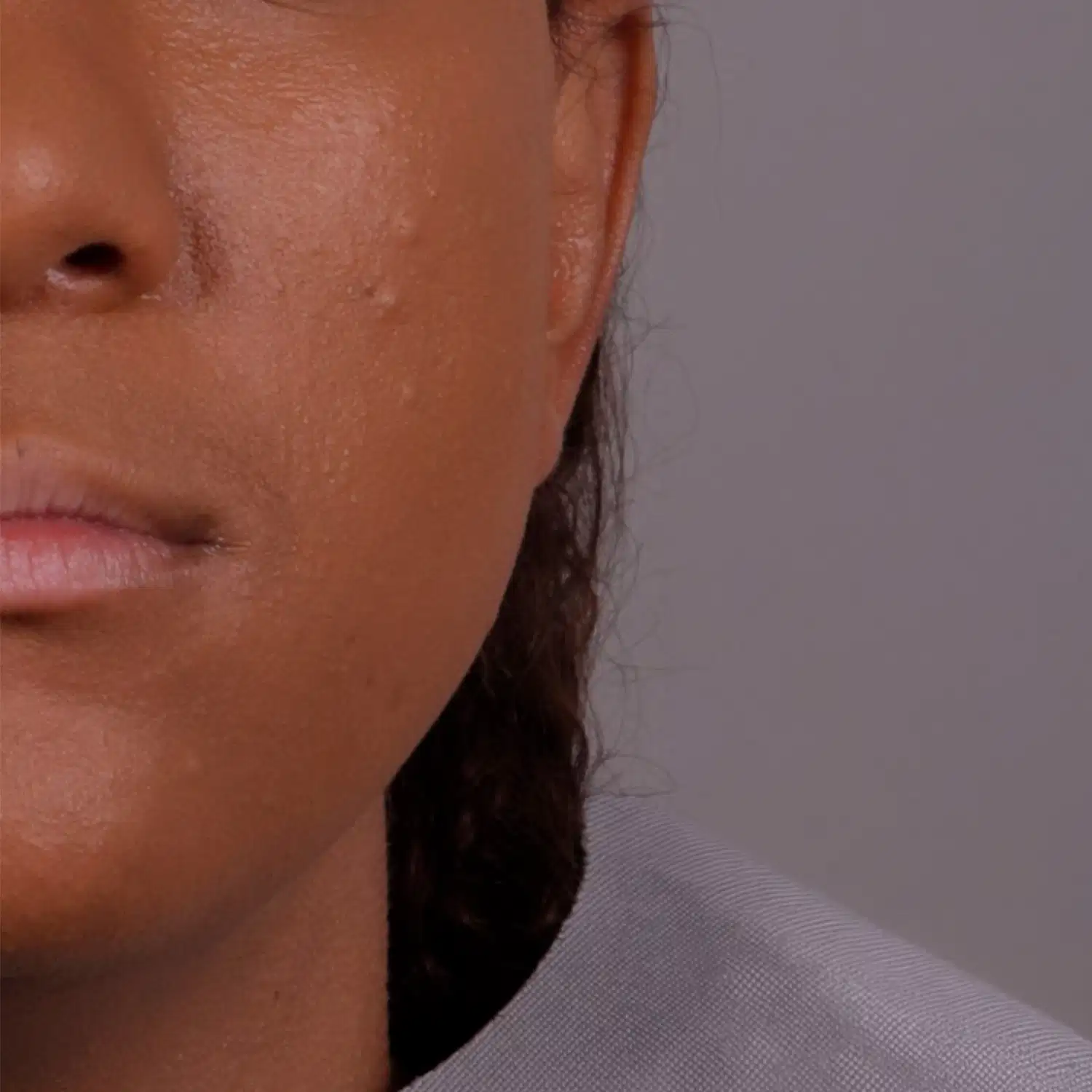 Imagem de close-up do quarto inferior esquerdo de um rosto feminino negro com um pouco de cabelo longo aparente próximo da nuca em um fundo cinza.
