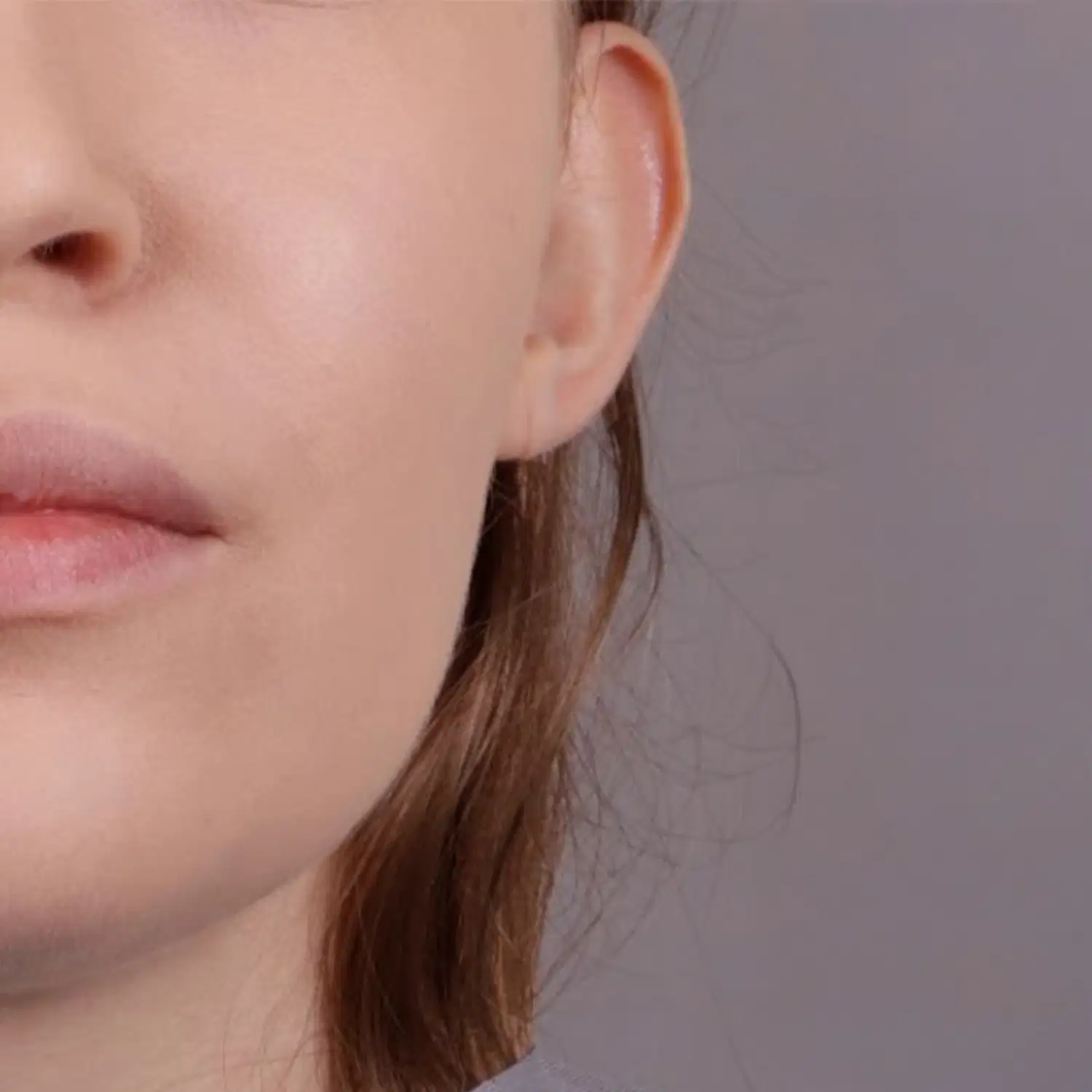 Imagem de close-up do quarto inferior esquerdo de um rosto feminino branco com mecha de cabelo ruivo e comprido aparente em um fundo cinza claro.