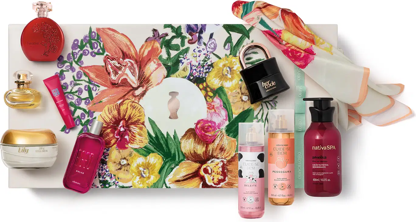 A imagem mostra uma superfície branca com arranjo de itens de perfumaria e cuidados pessoais, incluindo frascos, caixas com flores e folhagens estampadas e embalagens variadas dos produtos o Boticário.