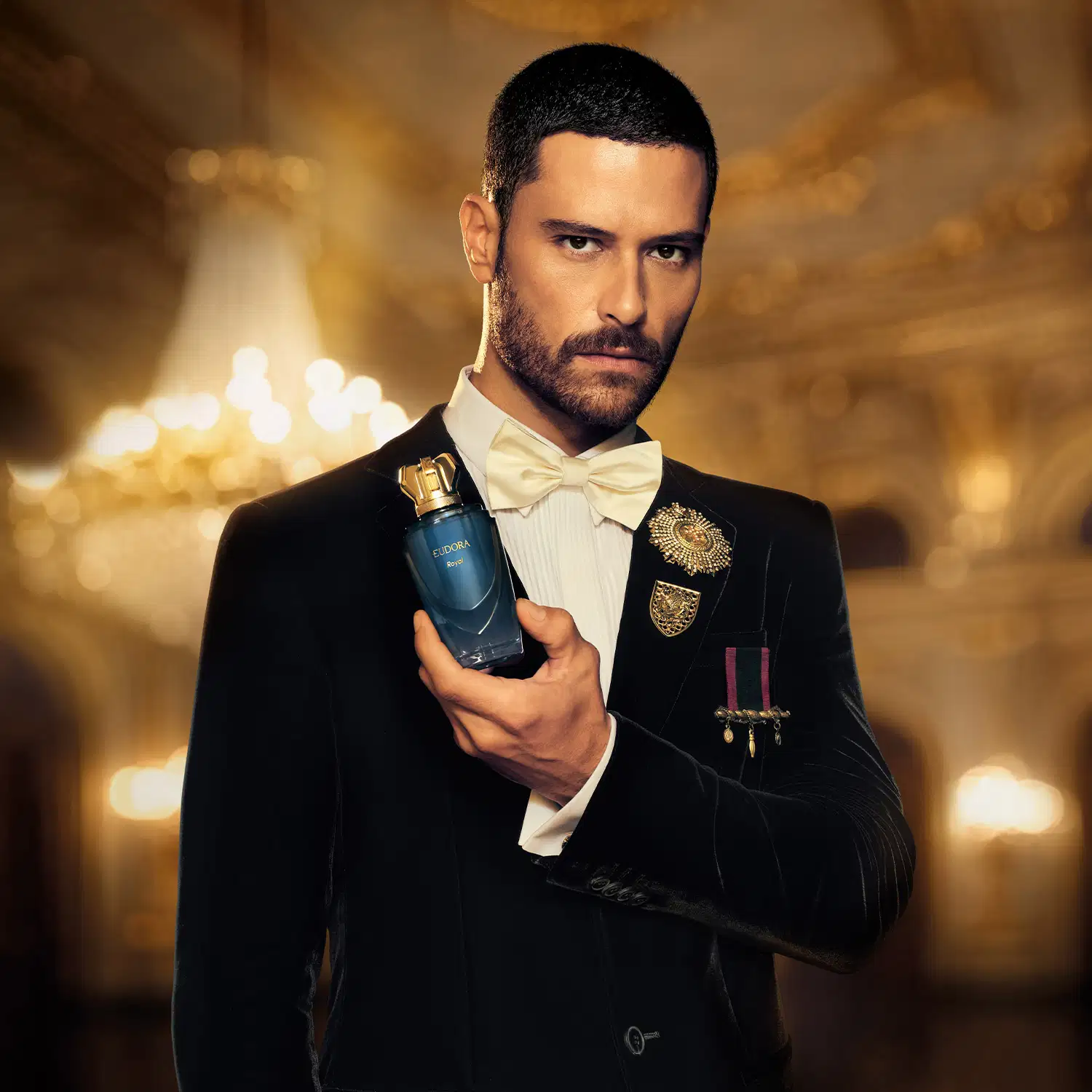 O homem elegantemente vestido em um terno preto segura um frasco de desodorante colônia da marca Eudora em um ambiente luxuoso e dourado, sugerindo uma ocasião sofisticada e da realeza.