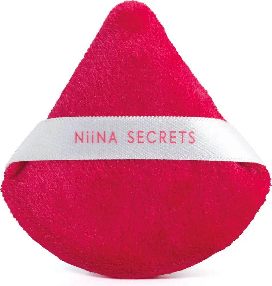 Esponja de maquiagem triangular de gota de cor vermelha intensa em material aveludado. Possui uma faixa branca com o texto Niina Secrets. O produto tem aparência macia e compacta.