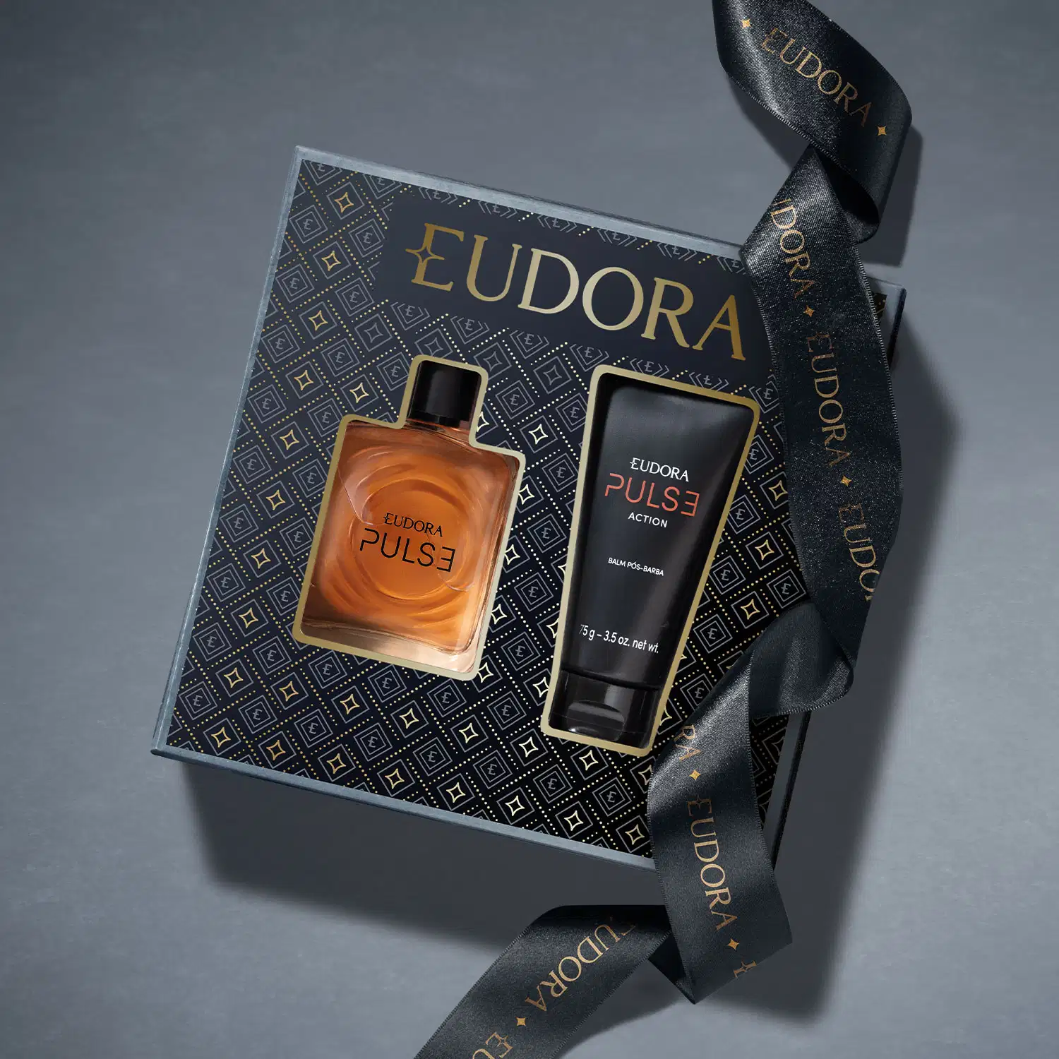 Caixa que contém os produtos Eudora Pulse vista de cima, em fundo cinza acompanhada de uma bela fita preta com logo EUDORA em dourado. A caixa é preta e estampada com padrão geométrico dourado apresentando a imagem dos produtos na sua parte frontal.