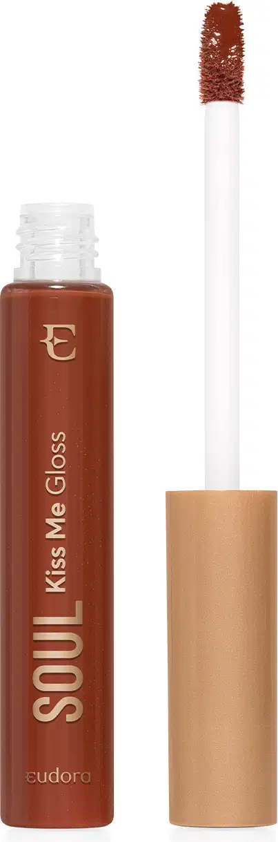 Frasco de vidro transparente contendo gloss marrom caramelo achocolatado. Rótulo com o nome do produto e da marca em letras douradas sobre fundo transparente do frasco e marrom do produto. Aplicador de espuma em formato de pincel firme. Tampa dourada