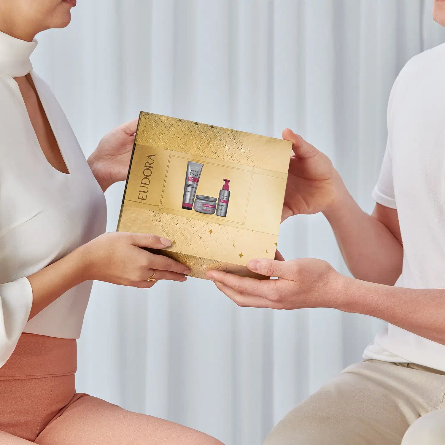 A imagem mostra um homem e uma mulher segurando uma caixa dourada, como se estivesse entregando um presente.