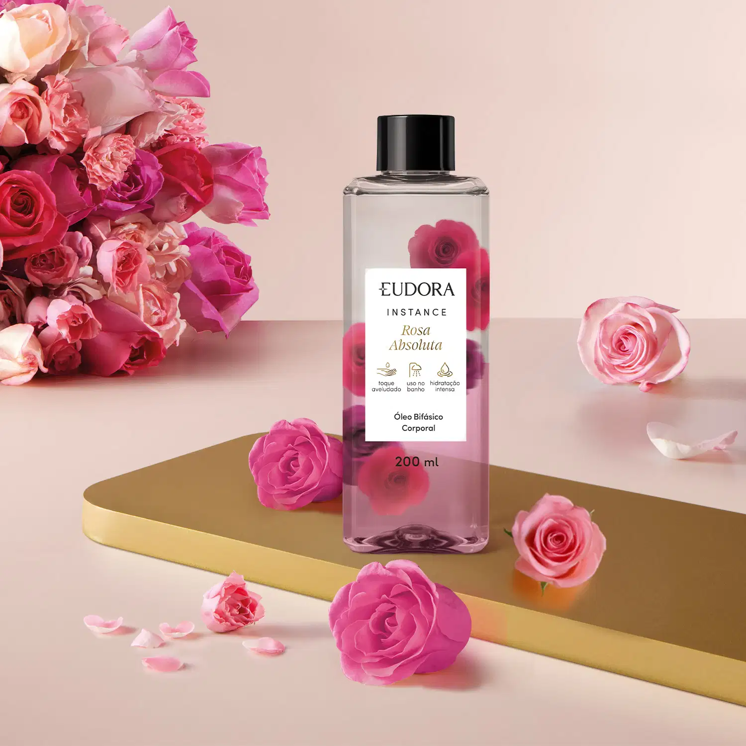 O frasco do Óleo Bifásico Instance Rosa Absoluta é transparente, com um rótulo preto e branco, e contém um líquido claro. O produto está posicionado em um ambiente com rosas rosa, criando uma composição visual harmoniosa.