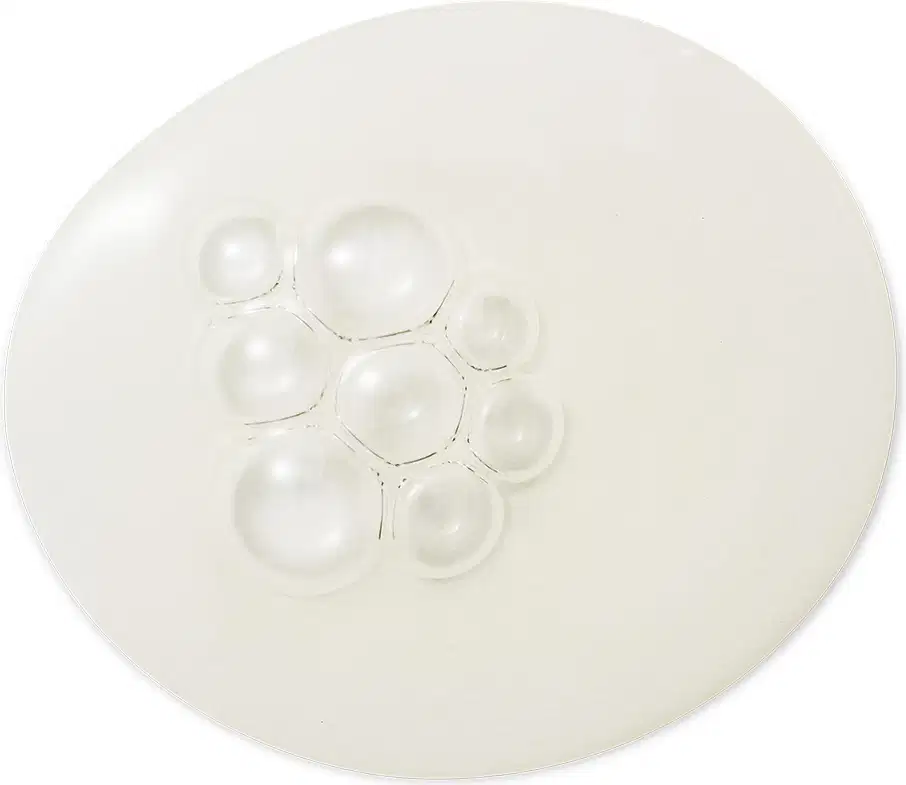 Textura transparente e brilhante de um item de skincare, com pequenas bolhas de ar distribuídas uniformemente sobre uma superfície lisa e clara.