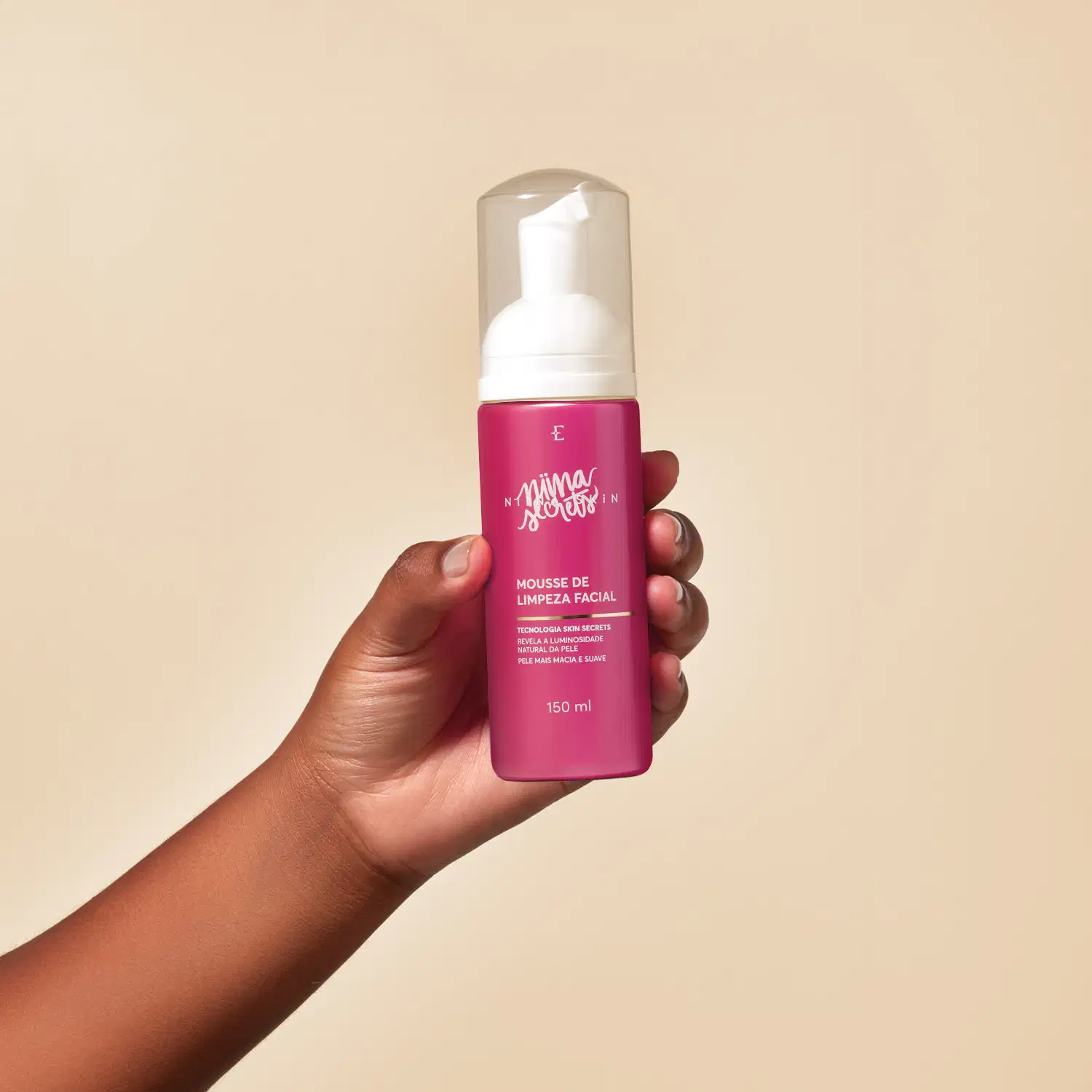 Produto de limpeza facial da marca Niina Secrets, em embalagem rosa, sendo segurado por uma mão em ambiente neutro de fundo bege. O produto é apresentado como uma mousse de limpeza facial com tecnologia skin secrets.