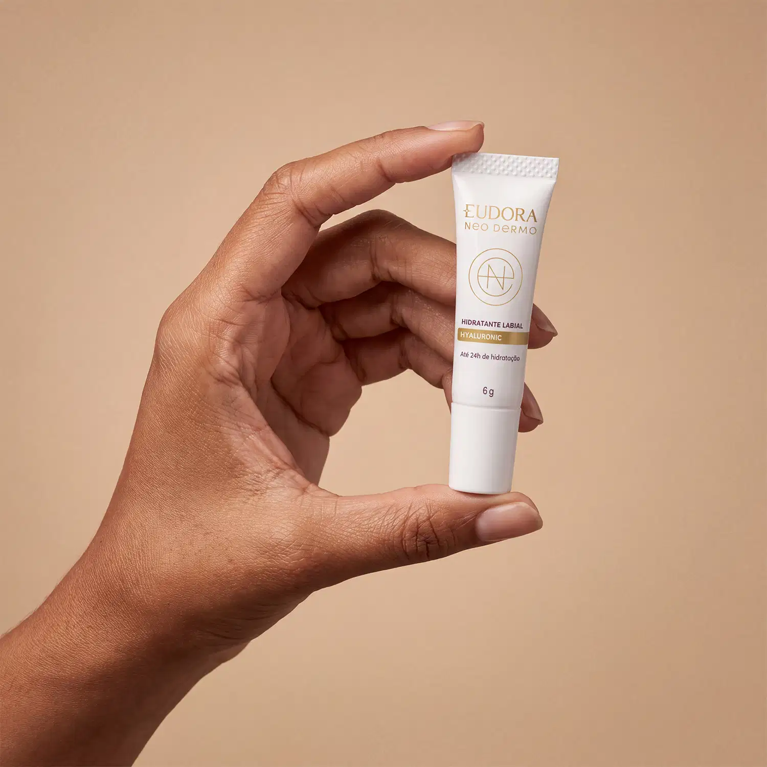 Bisnaga branca de hidratante labial da marca Neo Dermo, com texto em dourado "Hidratante Labial Hyaluronic" e logotipo da marca. O produto é segurado por uma mão feminina, indicando a proporção do tamanho.