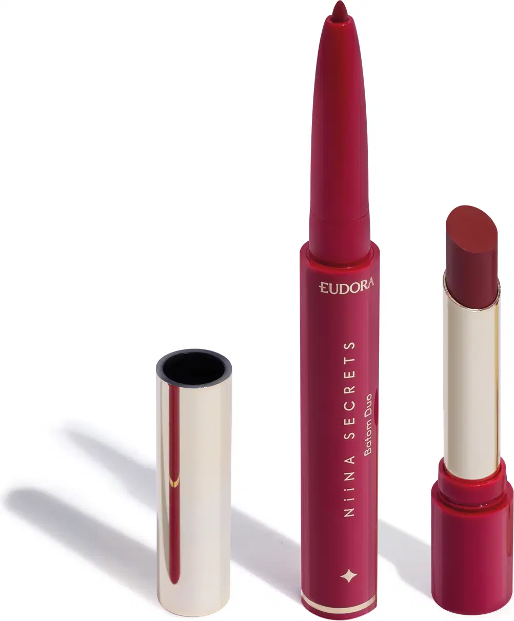 O produto apresentado na imagem é um batom da marca Niina Secrets Eudora, de tom marrom avermelhado fechado. São dois produtos em um: uma lapiseira delineadora com a ponta afiada e o batom em formato stick, com embalagem também rosa e detalhes dourados.