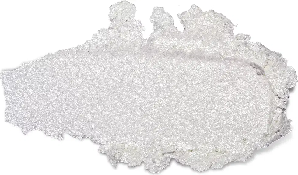 Textura do produto Iluminador Glam. Trata-se de um aglomerado de cristais brancos e brilhantes, com uma textura granulada e irregular. Não há embalagem ou rótulo visível na imagem, apenas o próprio produto.