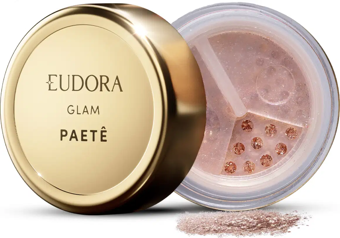 O produto apresentado é um Glitter da linha Glam Eudora. A embalagem é redonda, com uma tampa dourada. O glitter está contido em um recipiente transparente, permitindo visualizar seu conteúdo, que parece ser um pó de tonalidade rosada com pequenos brilhos