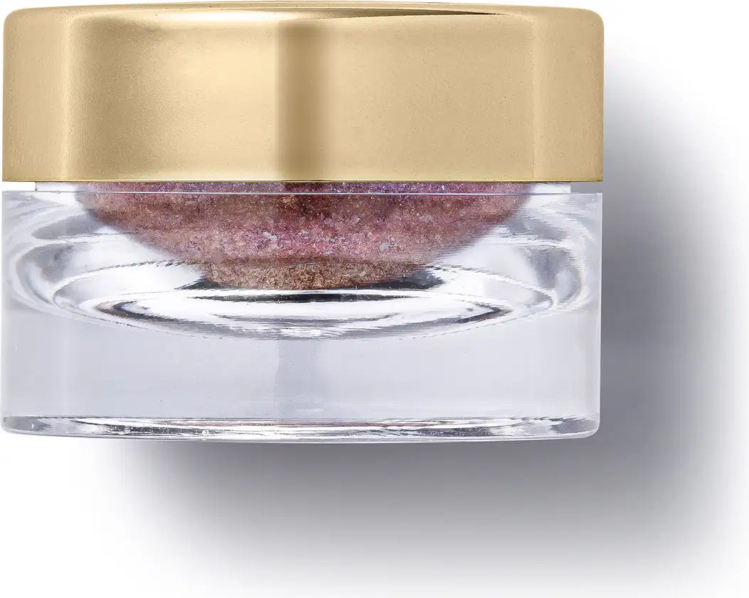 O produto apresentado é um pote transparente com uma tampa dourada. Dentro do pote, há uma substância de cor rosa. A embalagem possui um design elegante e minimalista, com a tampa dourada contrastando com o transparente.
