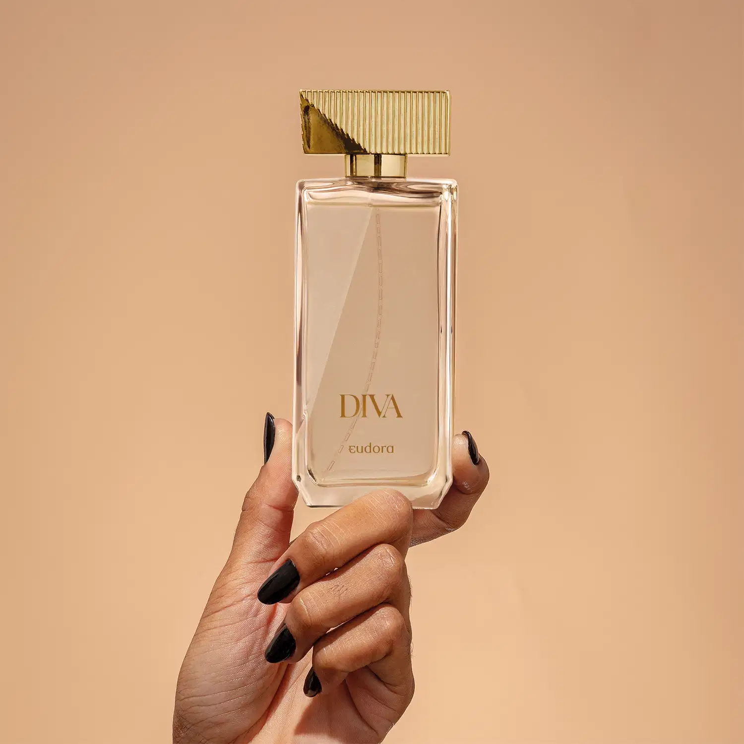 Frasco do Desodorante Colônia Diva da marca Eudora, com design elegante e sofisticado sendo segurado por uma mão feminina. Embalagem de vidro transparente com tampa dourada e detalhes verticais. 