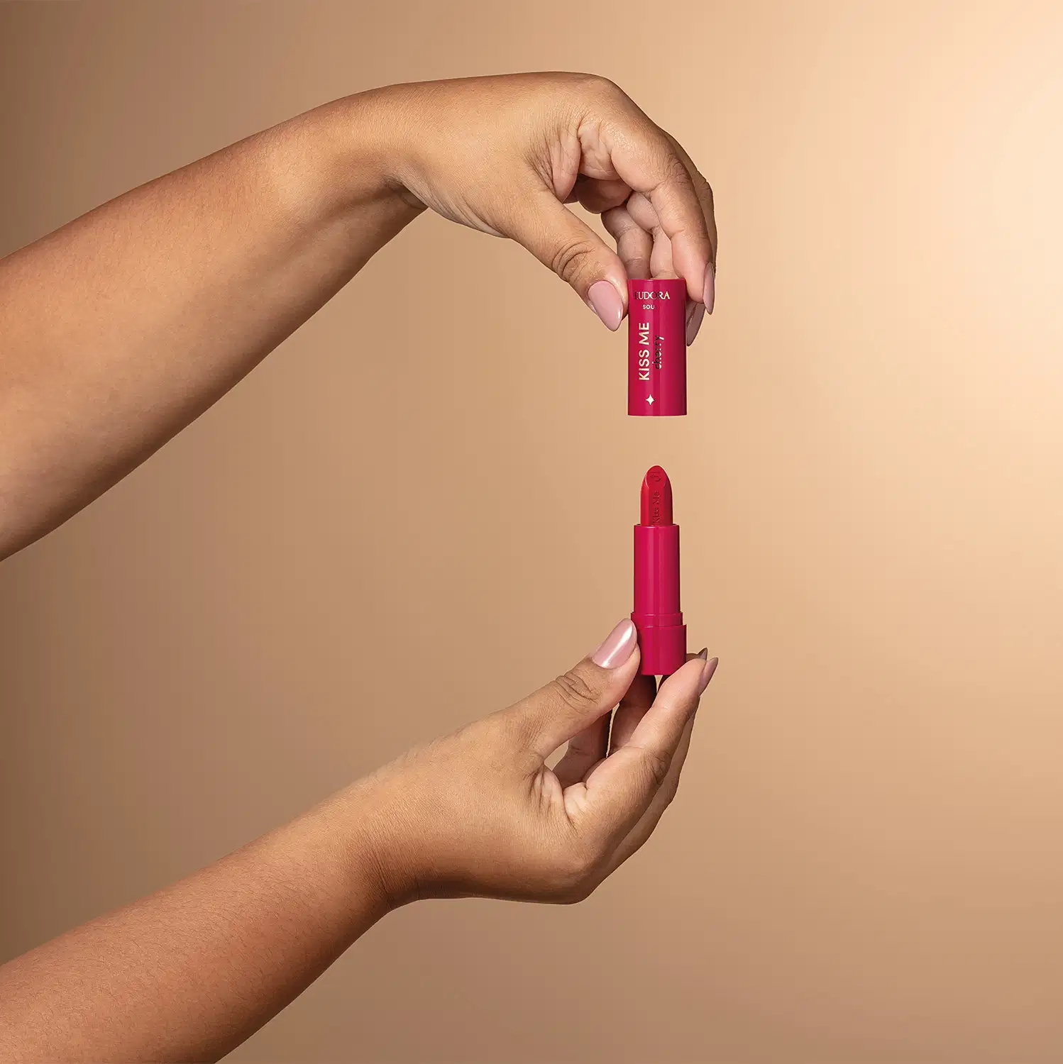 A imagem mostra um batom vermelho em formato de tubo, com a marca "Eudora" impressa no produto. Uma mão está segurando o produto aberto, coma tampa na parte de cima, mostrando o formato interno do batom.
