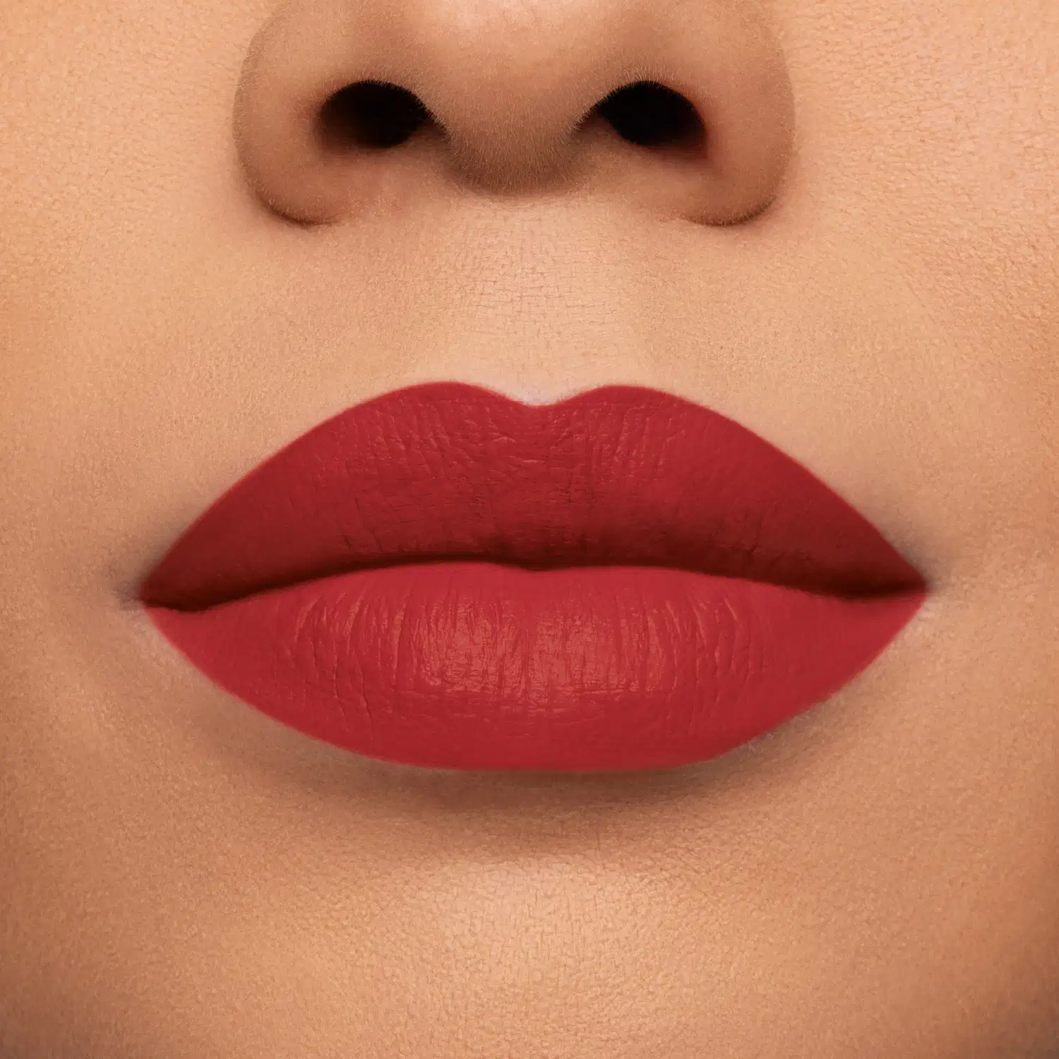 Foto com foco na boca da modelo com o produto Batom. Acabamento matte e uma cor predominante de vermelho vivo. A superfície do batom é lisa e opaca, com uma textura matte.
