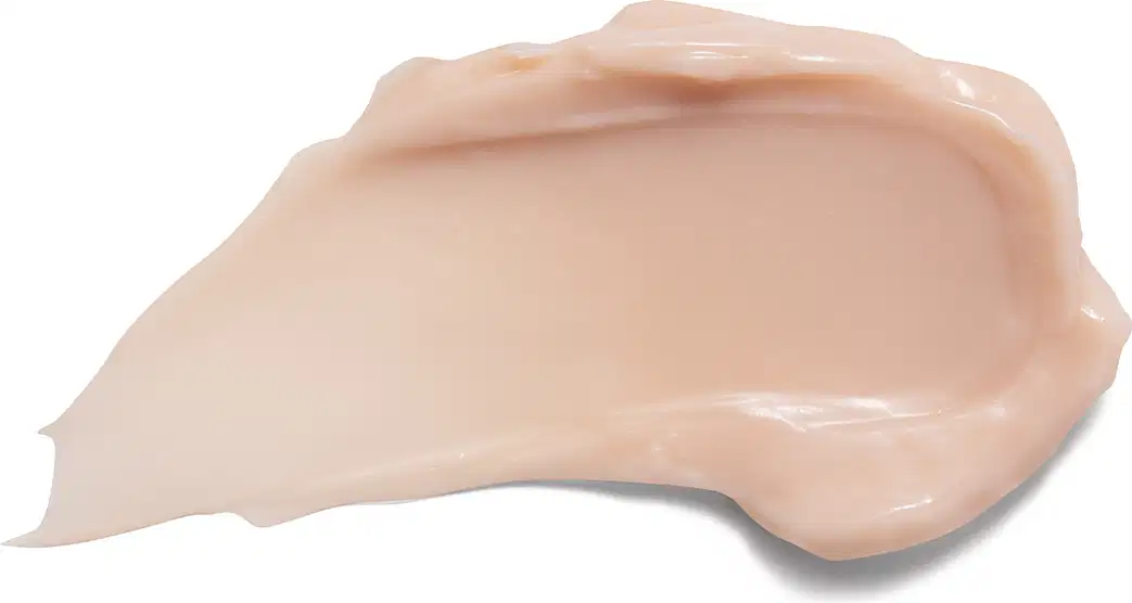O produto apresenta uma textura cremosa, de cor bege clara, com aparência suave e brilhante, sugerindo uma consistência macia e hidratante.