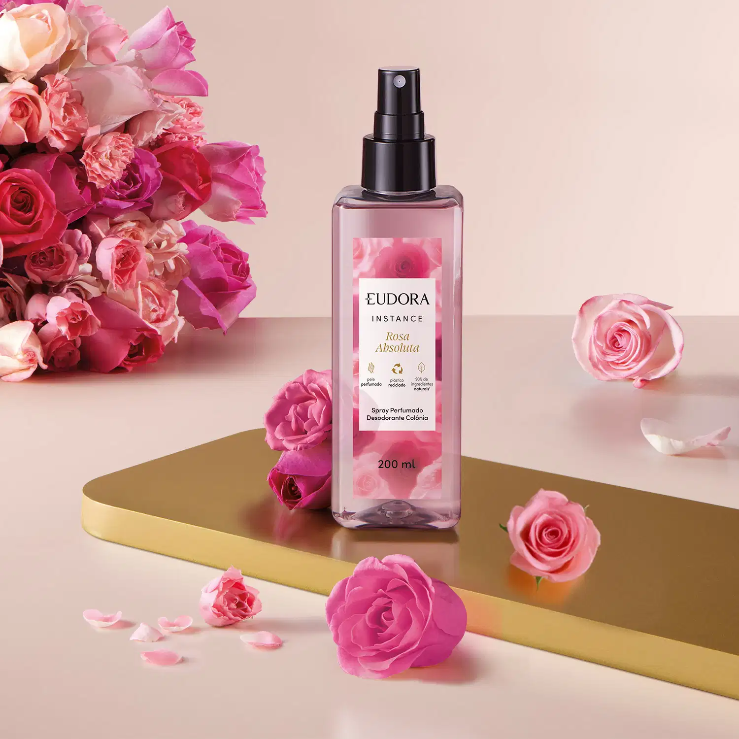 O frasco é preto com um borrifador, e o líquido dentro é de uma tonalidade rosada. O produto está posicionado em um cenário com rosas frescas de diversas cores, incluindo rosa, vermelho e salmão, criando uma composição visual elegante e delicada.